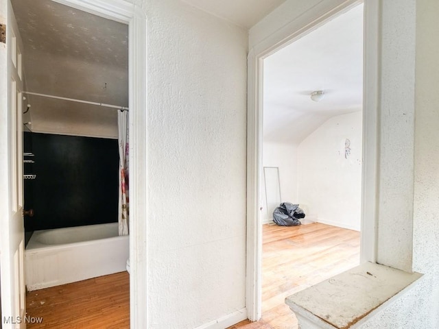 corridor with vaulted ceiling, wood finished floors, and a textured wall