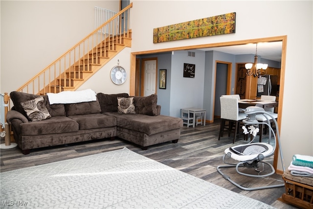 living area featuring visible vents, wood finished floors, stairway, a high ceiling, and an inviting chandelier