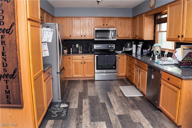 kitchen with decorative backsplash, appliances with stainless steel finishes, dark stone counters, and dark wood-style flooring