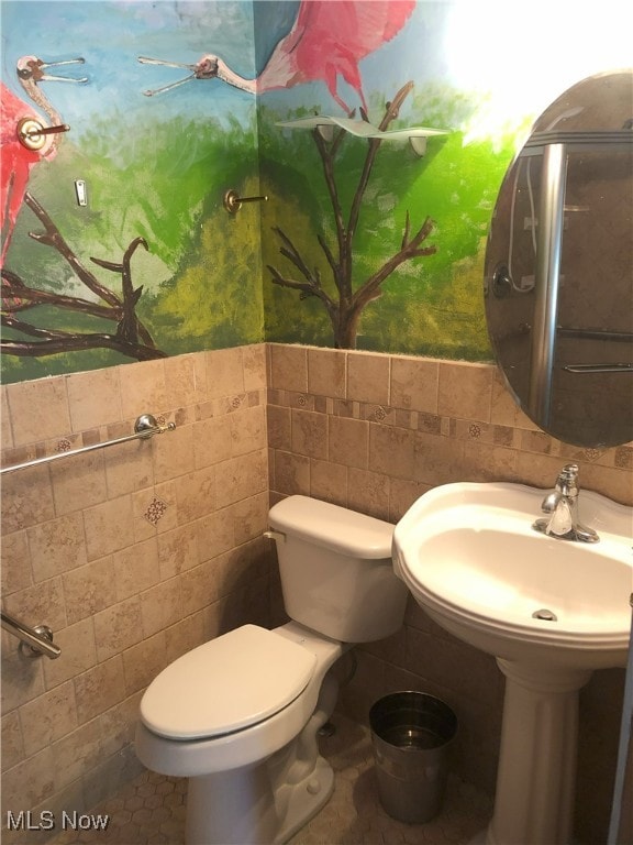 bathroom with a sink, toilet, and tile walls