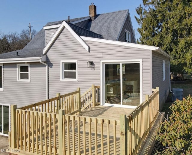 rear view of property featuring a shingled roof, a wooden deck, cooling unit, and a chimney