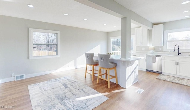 kitchen featuring a breakfast bar area, a sink, white cabinets, light wood-style floors, and stainless steel dishwasher