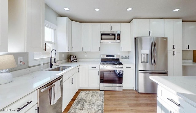 kitchen featuring light stone countertops, a sink, stainless steel appliances, light wood-style floors, and white cabinetry