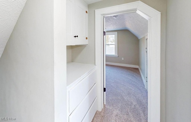 corridor featuring baseboards, lofted ceiling, light colored carpet, and a textured ceiling