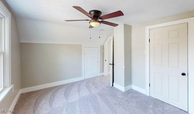 unfurnished bedroom featuring vaulted ceiling, carpet, baseboards, and a textured ceiling