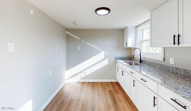 kitchen with light wood-style flooring, light stone countertops, baseboards, and a sink