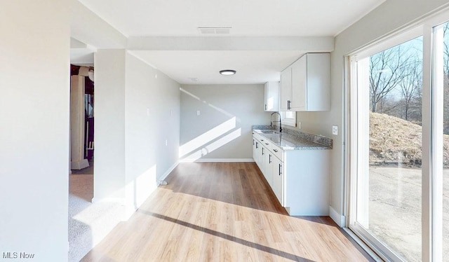 kitchen with wood finished floors, visible vents, light stone countertops, a sink, and white cabinetry