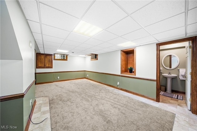 finished below grade area featuring a sink, a paneled ceiling, baseboards, and carpet flooring