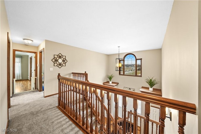 corridor featuring an upstairs landing, an inviting chandelier, baseboards, and carpet floors