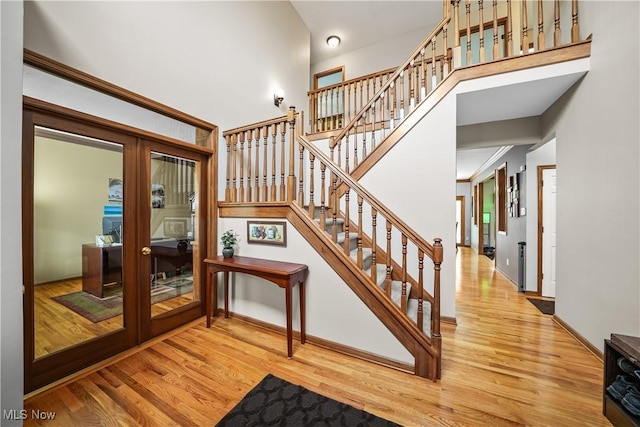 stairway featuring french doors, baseboards, wood finished floors, and a towering ceiling