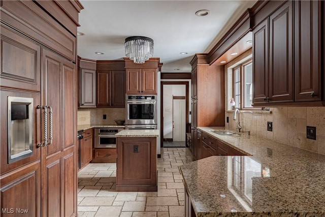 kitchen with stone tile flooring, a notable chandelier, light stone countertops, and a sink