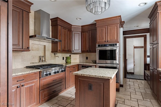 kitchen with stone tile floors, light stone counters, appliances with stainless steel finishes, wall chimney range hood, and tasteful backsplash