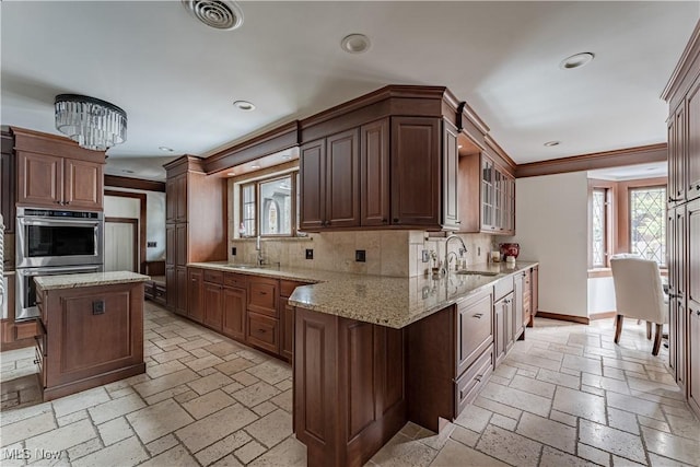 kitchen featuring visible vents, a sink, backsplash, stone tile flooring, and baseboards