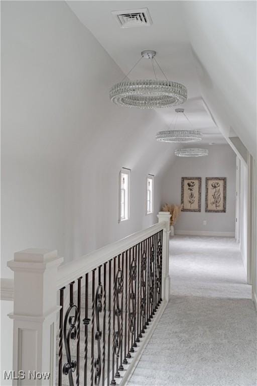 hallway featuring visible vents, an upstairs landing, carpet floors, and vaulted ceiling