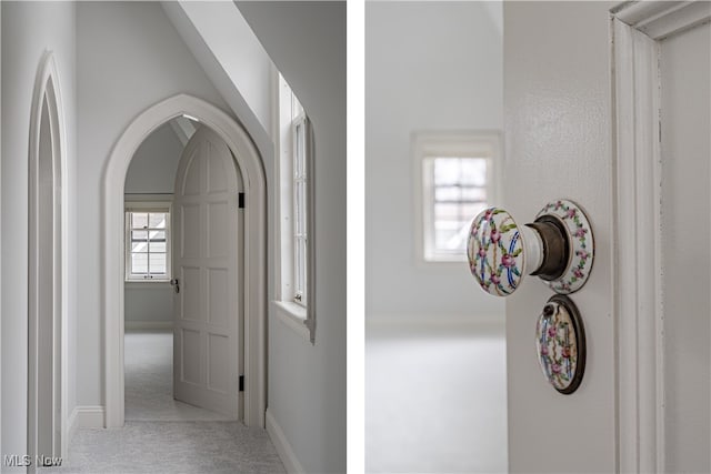 hallway featuring arched walkways, light colored carpet, and baseboards