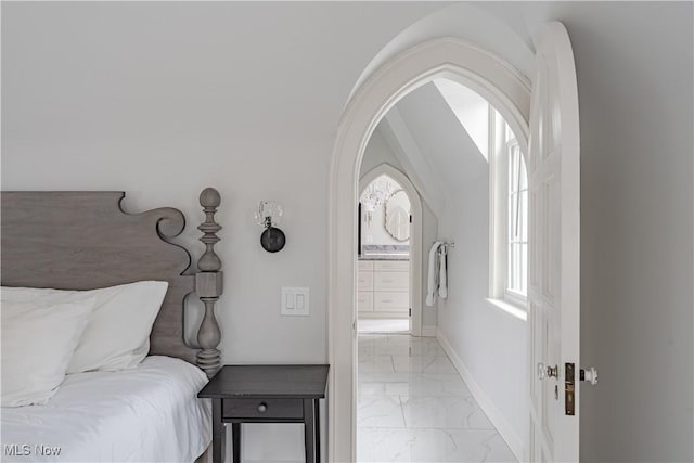 bedroom featuring arched walkways, marble finish floor, connected bathroom, and baseboards