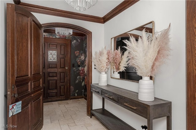 entryway with baseboards, an inviting chandelier, arched walkways, ornamental molding, and stone tile flooring