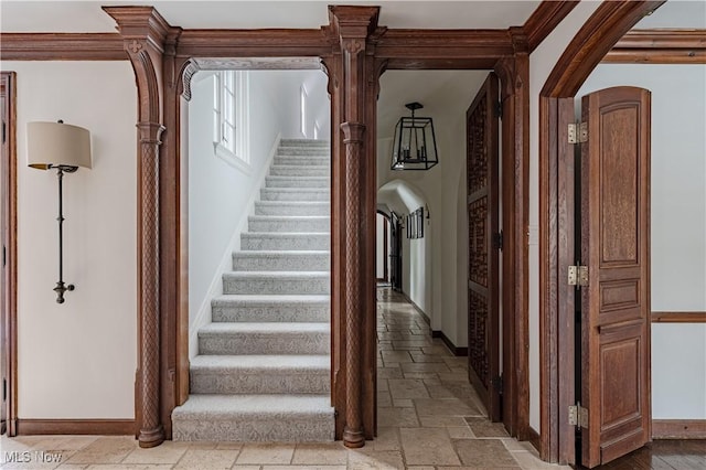 staircase with stone tile floors, arched walkways, crown molding, and baseboards