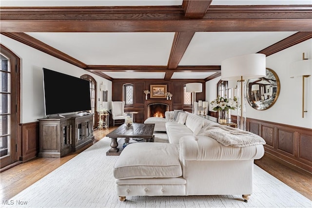 living room with beamed ceiling, light wood-style flooring, a wainscoted wall, and coffered ceiling