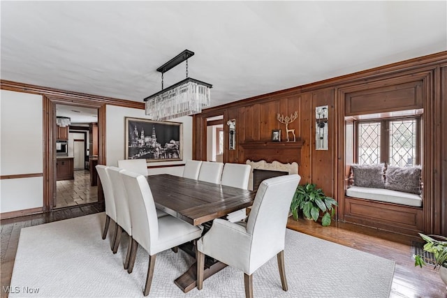 dining room with hardwood / wood-style floors, wooden walls, ornamental molding, and a chandelier