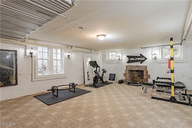 exercise room featuring a brick fireplace, carpet, and a textured wall