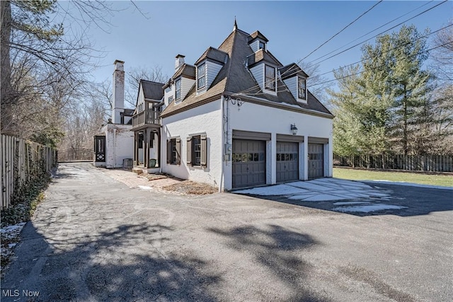 view of side of home featuring fence, driveway, stucco siding, a chimney, and a garage