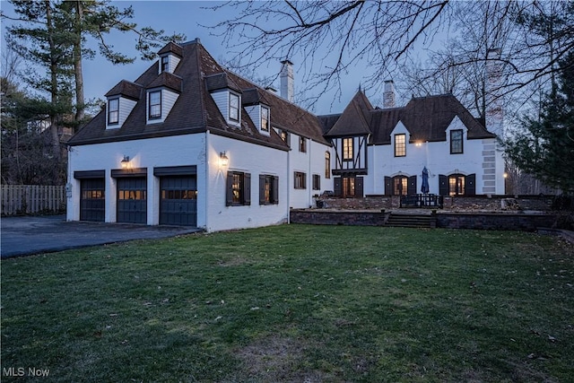 rear view of house featuring fence, a chimney, a garage, a yard, and driveway