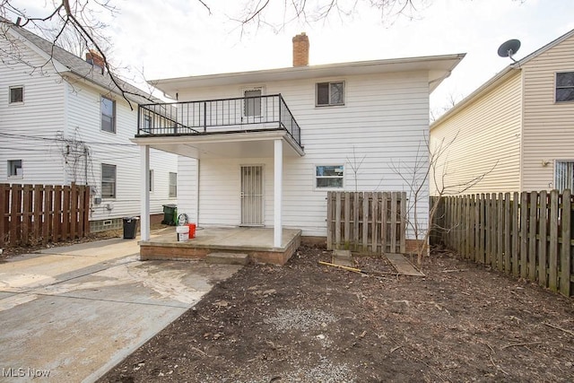 rear view of house with a patio, a balcony, a fenced backyard, and a chimney