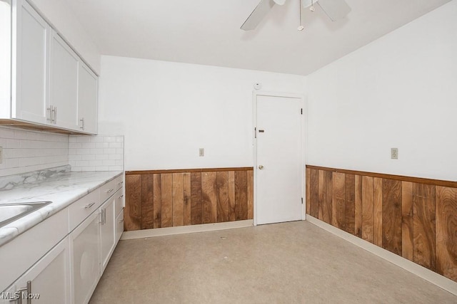 kitchen featuring wooden walls, finished concrete floors, ceiling fan, wainscoting, and white cabinetry