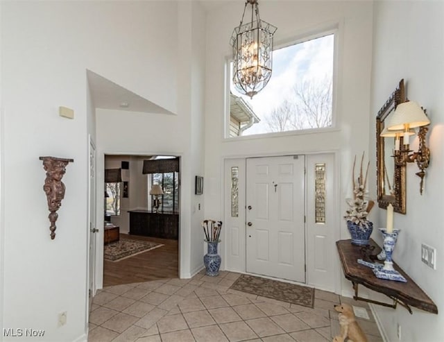 foyer featuring light tile patterned floors, a notable chandelier, a high ceiling, and baseboards