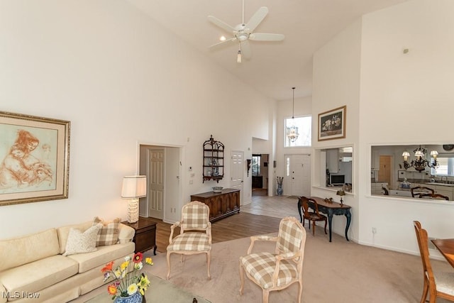 living area with ceiling fan with notable chandelier, high vaulted ceiling, and baseboards