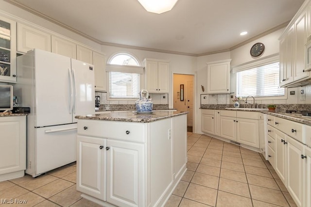 kitchen with a sink, a kitchen island, white cabinetry, freestanding refrigerator, and light tile patterned floors