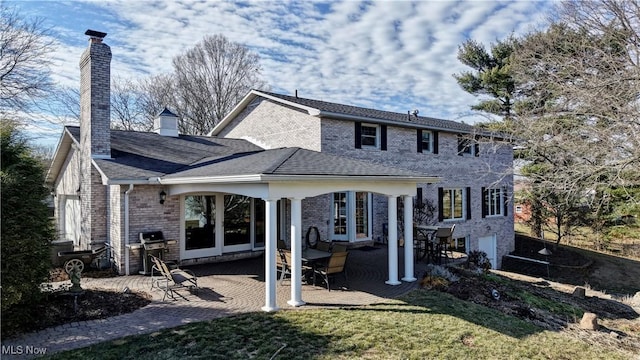 rear view of property featuring brick siding, a patio area, a chimney, and a lawn