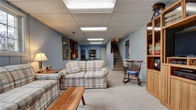 living area featuring a drop ceiling, stairway, and light colored carpet