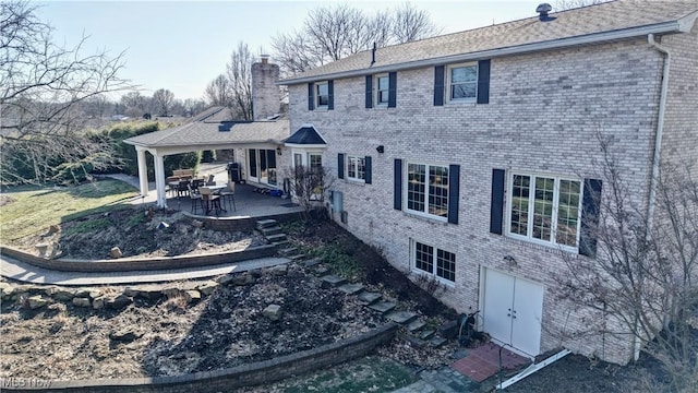 back of property with a patio, brick siding, and a chimney