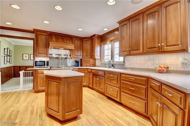 kitchen with a wainscoted wall, light wood-style flooring, ornamental molding, light countertops, and stainless steel microwave