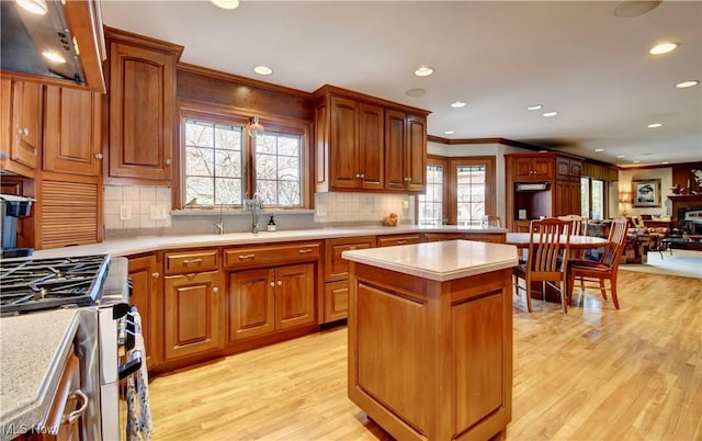 kitchen featuring gas stove, a kitchen island, ornamental molding, light countertops, and light wood-style floors