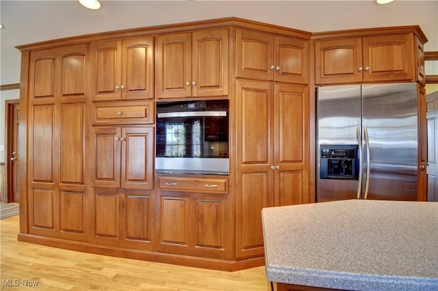 kitchen featuring brown cabinetry, light wood finished floors, appliances with stainless steel finishes, and light countertops