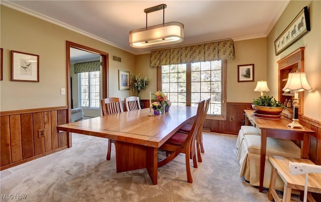 carpeted dining area with a wainscoted wall, wooden walls, visible vents, and ornamental molding