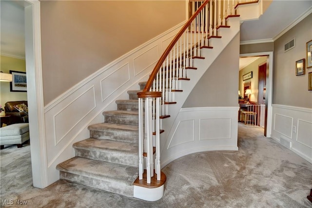 stairway featuring visible vents, carpet floors, ornamental molding, and a decorative wall