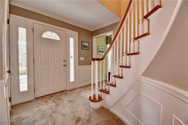 carpeted entryway with stairs, ornamental molding, wainscoting, and a decorative wall