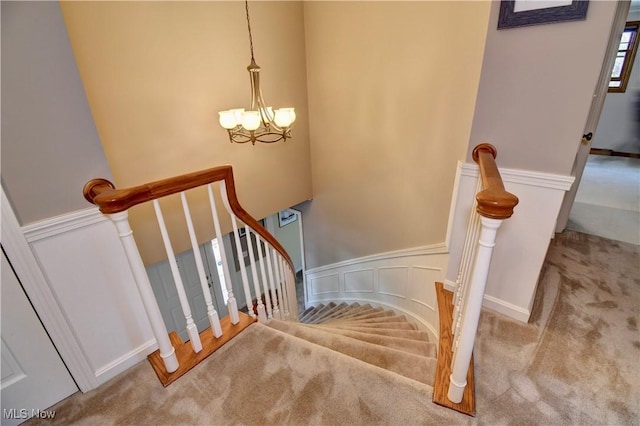 staircase featuring a decorative wall, carpet, a wainscoted wall, and a chandelier