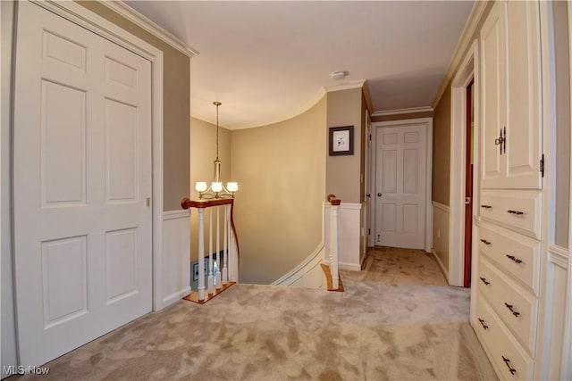 corridor with an upstairs landing, a notable chandelier, light colored carpet, and ornamental molding