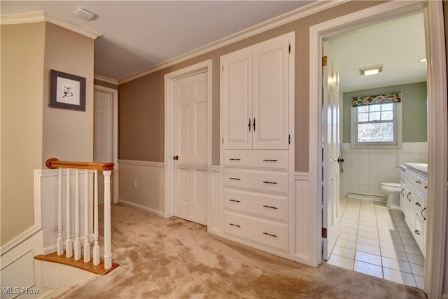 hallway with light tile patterned floors, wainscoting, crown molding, light colored carpet, and tile walls