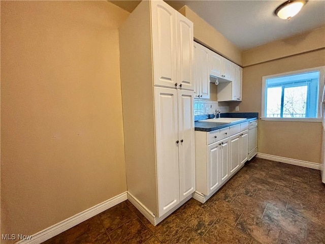 kitchen with tasteful backsplash, white cabinets, baseboards, and white dishwasher