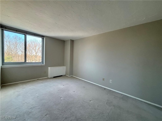 carpeted spare room with radiator, baseboards, and a textured ceiling