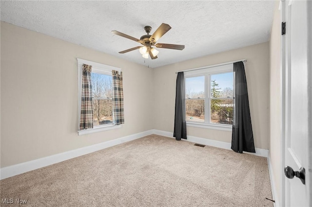 carpeted spare room featuring a textured ceiling, a ceiling fan, visible vents, and baseboards