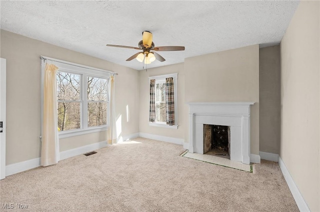 unfurnished living room featuring visible vents, a fireplace with flush hearth, carpet flooring, baseboards, and ceiling fan