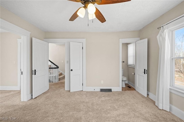 unfurnished bedroom with a textured ceiling, ensuite bath, baseboards, and light carpet