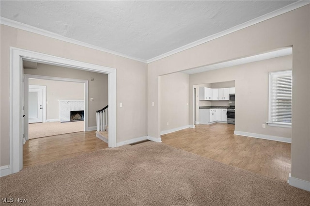 unfurnished living room featuring light colored carpet, a textured ceiling, baseboards, and ornamental molding